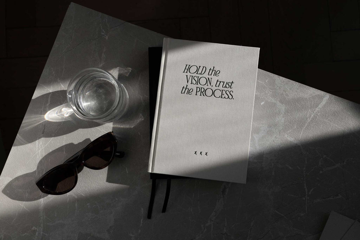 Notizbuch „Hold the Vision“ neben Sonnenbrille und Glas